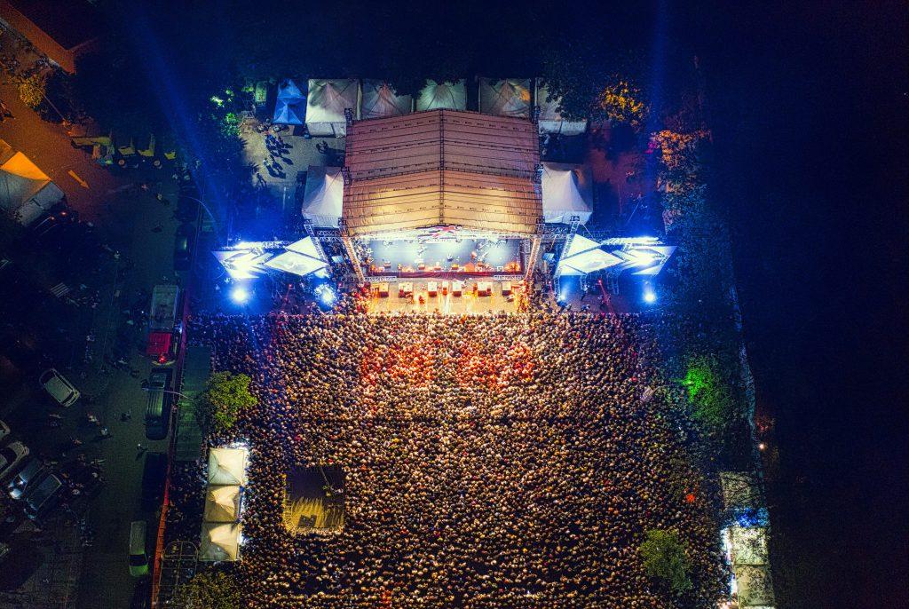A breathtaking aerial shot capturing a lively concert crowd at night with bright stage lights.